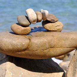 Sculpture de pierres empilées en arc sur un rocher, en bord de mer.
